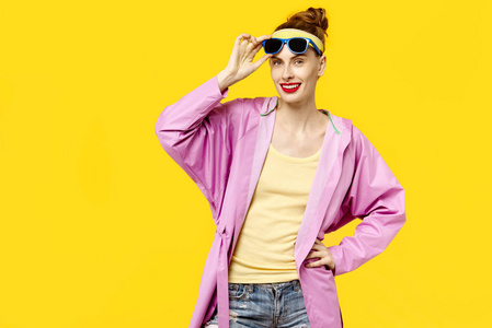 在黄色背景和粉红色外套和太阳镜的年轻妇女。色彩痴迷的概念。简约风格。时尚时尚