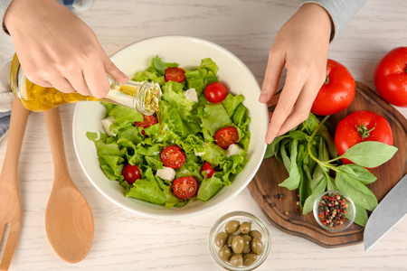 在桌上用新鲜蔬菜沙拉加入橄榄油的妇女