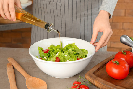 在桌上用新鲜蔬菜沙拉加入橄榄油的妇女