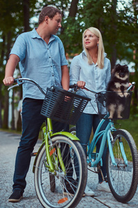 一个有吸引力的家庭穿着休闲衣服骑自行车与他们可爱的小斯皮茨狗