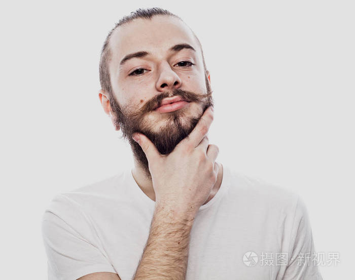 认真的.集中胡子男子身穿白色衬衫和耳环, 抚摸着他的下巴, 而思考