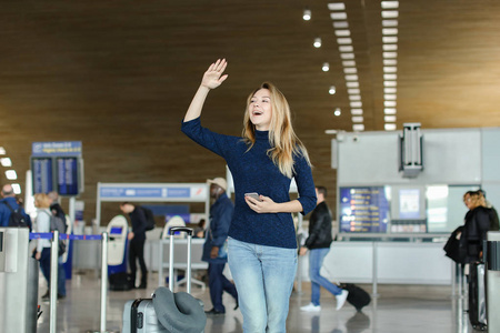 站在机场大厅的妇女智能手机, 手提箱和举手