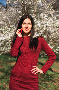 美丽的年轻黑发在公园里的长头发在春天在开花的树中间在红色礼服
