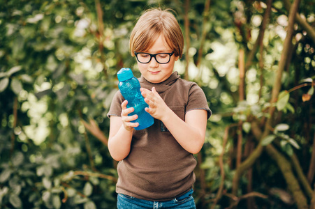 强壮, 聪明, 有趣的小男孩在户外玩耍, 戴着眼镜, 捧着一瓶水
