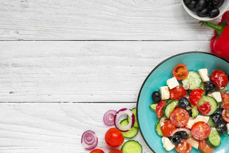 希腊沙拉与新鲜蔬菜, 羊乳酪和黑橄榄在一个板材与配料在白色木桌上