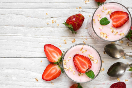 健康草莓酸奶燕麦和薄荷在玻璃与新鲜的浆果和勺子在白色的木桌上