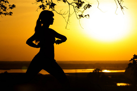 在夕阳下做体育锻炼的女人的剪影, 体育女性在领域, 体育和娱乐的概念