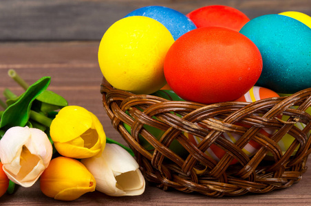 复活节彩蛋在柳条篮子, 红色和黄色郁金香在木板材