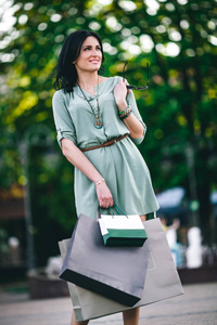 时髦的黑发在长袍站立与杯子和与购物在她的手在公园在夏天