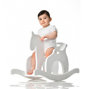 蹒跚学步的小女孩骑着摇摆椅上的玩具马在白色