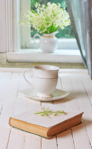 一杯黑色的咖啡或茶和书上的白色木制复古表和一束百合花在窗台上的