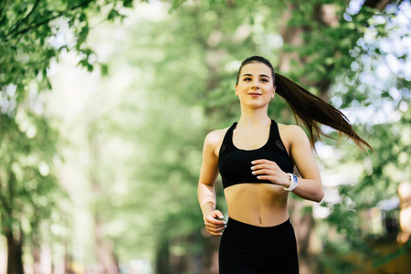 年轻的微笑运动的女人在公园里奔跑。健身女孩公园慢跑