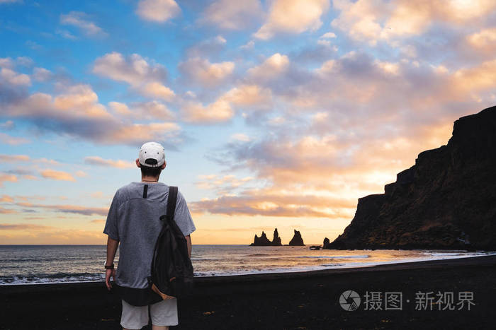 冰岛日落时, 一个背包的男人站在黑色沙滩上.