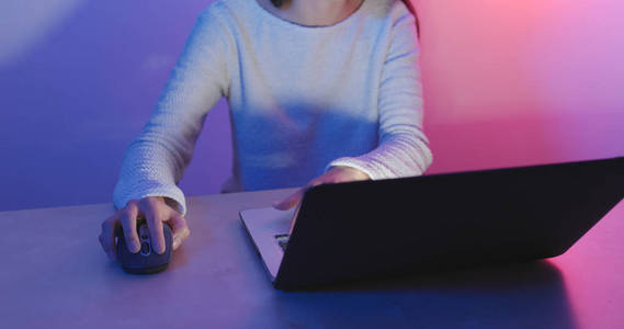 妇女工作在计算机和老鼠用蓝色和紫色光