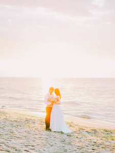 美丽的新婚夫妇在日落时分拥抱海滩