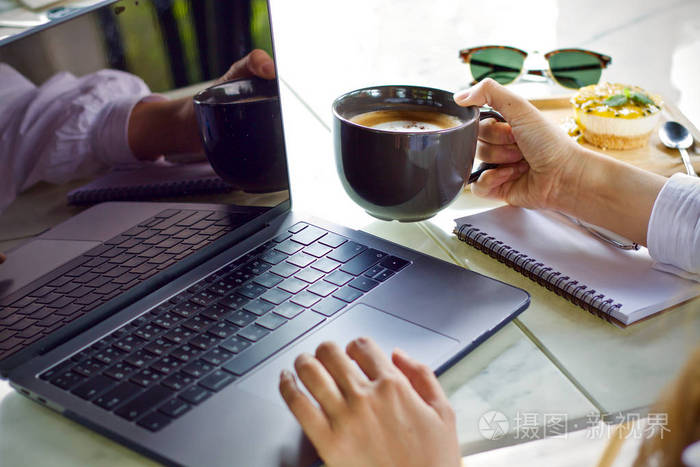 妇女使用膝上型电脑工作和喝咖啡杯热