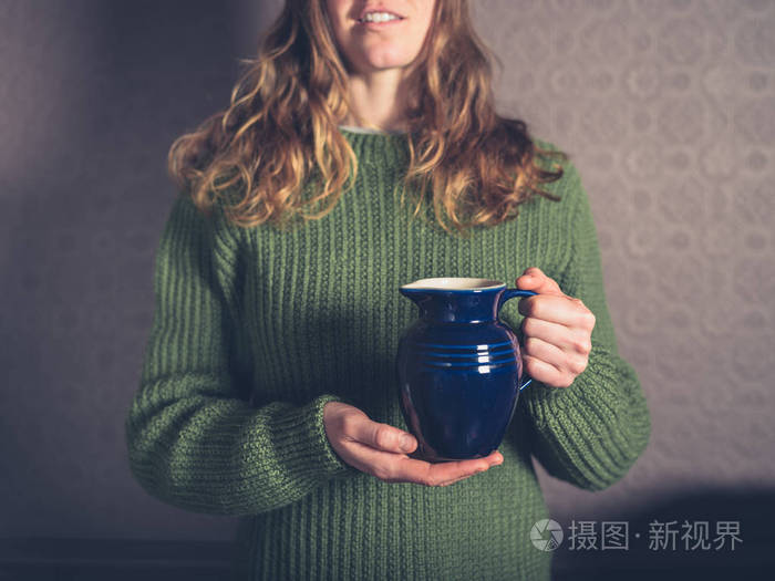 一个穿着跳线的年轻女子拿着一个陶瓷壶