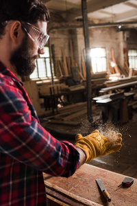 有胡子的工匠在保护谷歌和手套在锯木厂从手摇晃木头芯片