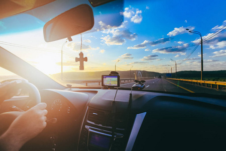司机的手与正统十字架和汽车驾驶员在挡风玻璃期间在高速公路上在日出