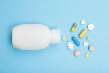 白色瓶与不同的药丸和胶囊在蓝色背景。顶部视图