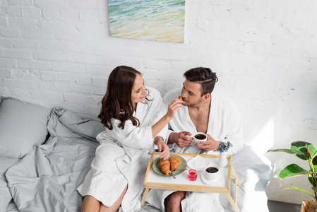 美丽的年轻夫妇在浴袍一起在床上吃早餐