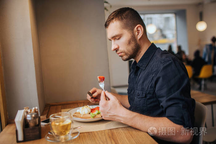 一张坐在餐桌旁吃饭的男人的照片.他在叉子上有一块西红柿.
