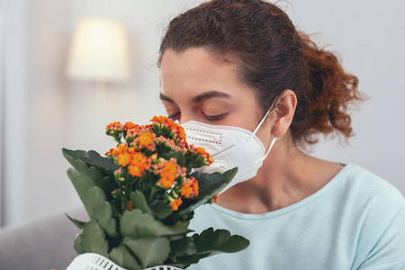 戴着呼吸面罩的年轻女孩嗅到一盆花的花朵