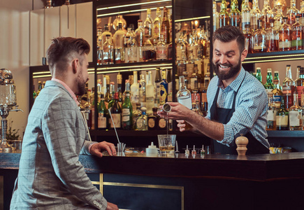 欢快时尚的野蛮酒保在衬衫和围裙服务的客户在酒吧柜台背景