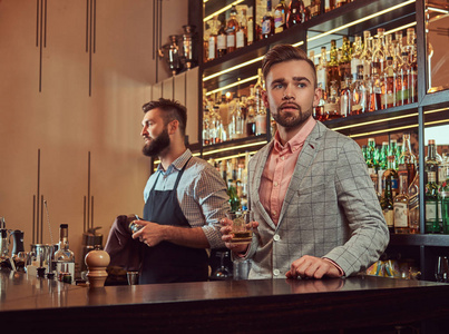 时尚英俊的男子在一个优雅的西装持有一杯威士忌在酒吧柜台背景