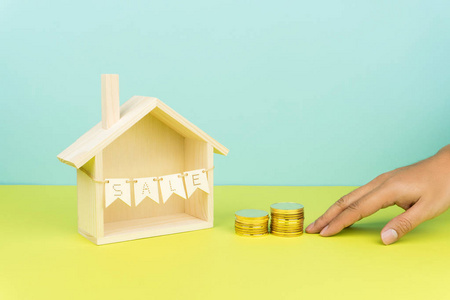 买房子的概念, 手推两堆金币向一个出售标志的木制房子模型