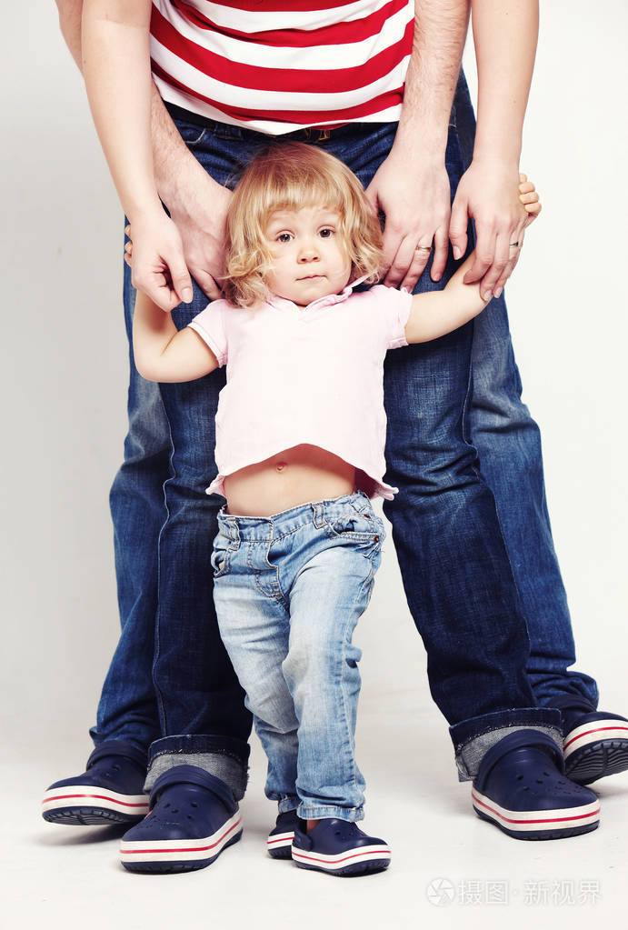 一个可爱的小女孩在衬衫和牛仔裤站在白色背景与她的父母的肖像