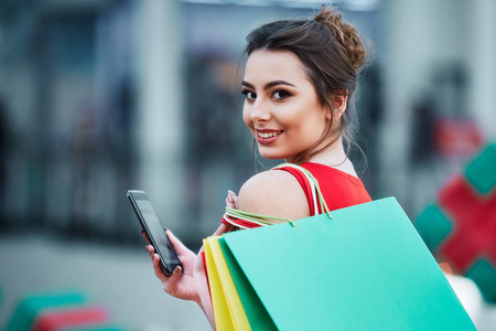 美丽的黑发年轻妇女与五颜六色的购物袋使用手机, 网上购物的概念