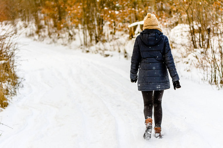 冬天的妇女在雪路, 女孩在黑外套, 后面看法在公园