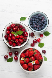 新鲜的夏日浆果。樱桃, 蓝莓和草莓在碗上白色木质背景。顶部视图