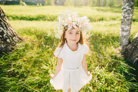 快乐的年轻女孩与她的头上的花朵花圈和白色的礼服微笑愉快地