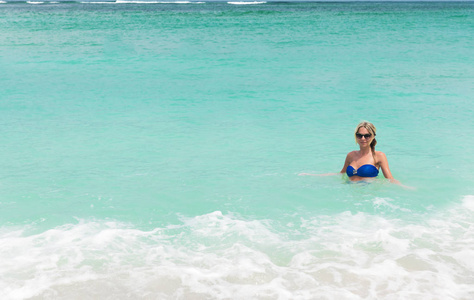 年轻漂亮的金发女人在白色的热带海滩上的蓝色比基尼