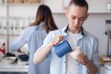 有时髦发型的男士们在工作时站在 cappuchino 做饭。他在咖啡里倒牛奶。