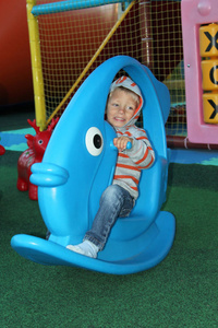 小男孩在操场上用鱼的形式在蓝色玩具上摇摆