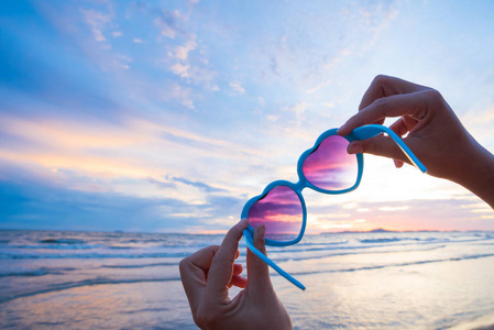夏季假期和度假概念的背景下, 女性手捧太阳镜在海上和沙滩上的心脏形状上的软聚焦
