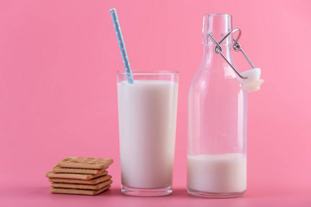 在粉红色背景下的新鲜牛奶和饼干的玻璃瓶。多彩简约。健康乳制品与钙的概念