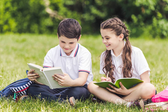 可爱的小学生一起做作业, 坐在公园的草地上照片-正版商用图片0uk1wz