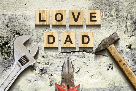 爱爸爸在木制立方体与工作工具在旧的老式混凝土墙上题词。父亲节快乐的概念。问候和礼物。假期