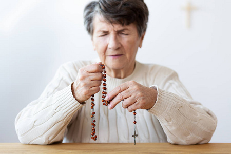 特写在一个集中的祖母的手祈祷与红色念珠在教会里