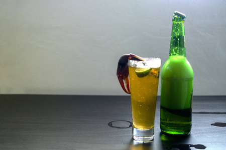 一瓶啤酒在桌上, 一只螃蟹的爪在杯子里照片