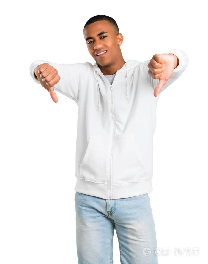深色皮肤的年轻人穿着白色的运动衫, 双手拿着拇指向下。孤立白色背景上的负表达式