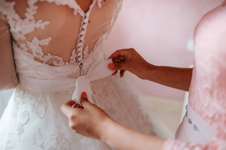 伴娘在婚礼前帮新娘系上婚纱礼服。豪华婚纱礼服关闭。最好的早晨。婚礼理念