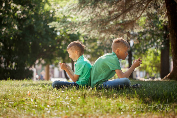 两个孩子的兄弟玩游戏的智能手机与兴奋, 而坐在草地上公园