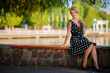 一个穿着漂亮的年轻女子坐在池塘边的长凳上。