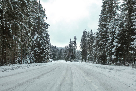 冬季森林公路覆盖着冰雪, 远处的汽车朝相反的方向走来。危险驾驶条件