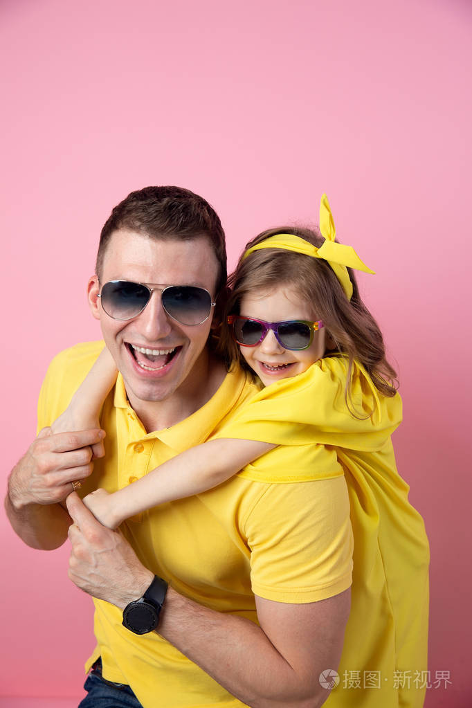 可爱的爸爸和女儿在黄色和太阳镜拥抱彩色粉红色的背景.暑期理念
